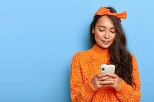 jeune-femme-pull-orange-discutant-son-smartphone